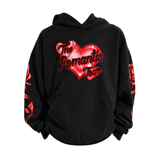 A black pullover hoodie featuring a large red heart graphic on the chest with the text 'The Romantic Tour' in black script. Red rose illustrations are printed down both sleeves.